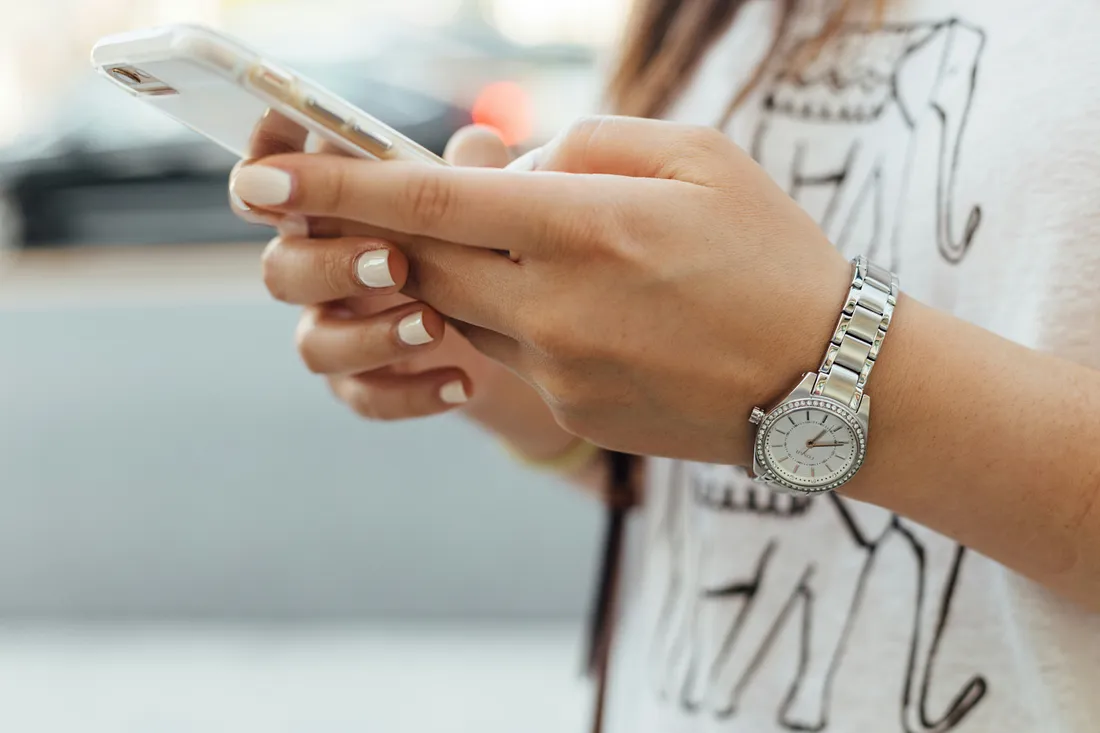 A woman with beautiful nails and a watch writing down something on her phone