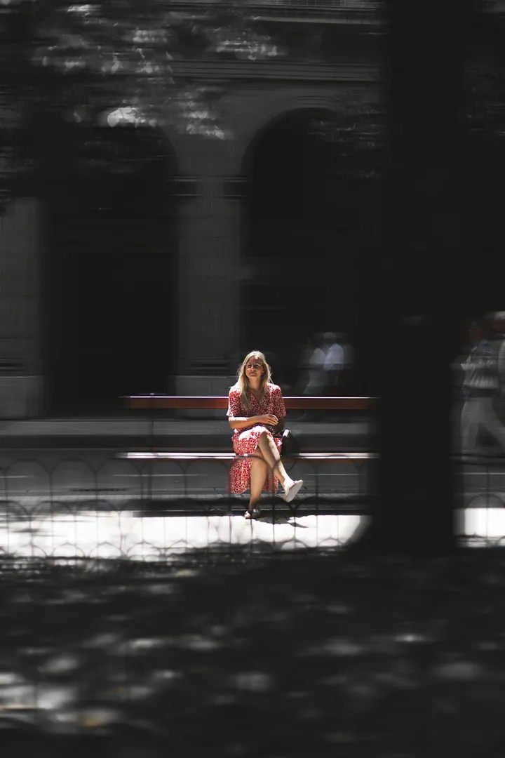 Girl in pink dress sitting on a park bench.