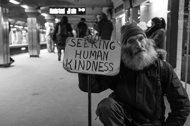 Man on a metro station with a sign that says, Seeking human kindness