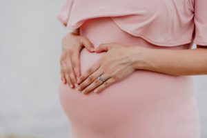 An expectign woman with a pink dress making a heart shape sign with her hands over her belly