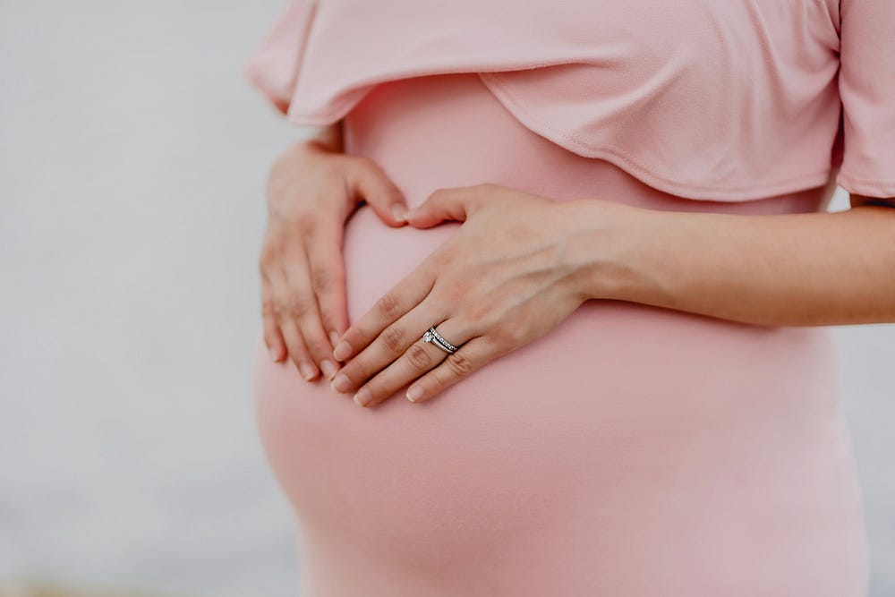An expectign woman with a pink dress making a heart shape sign with her hands over her belly