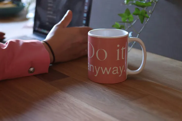Pink cup on a wooden table that says, do it anyway
