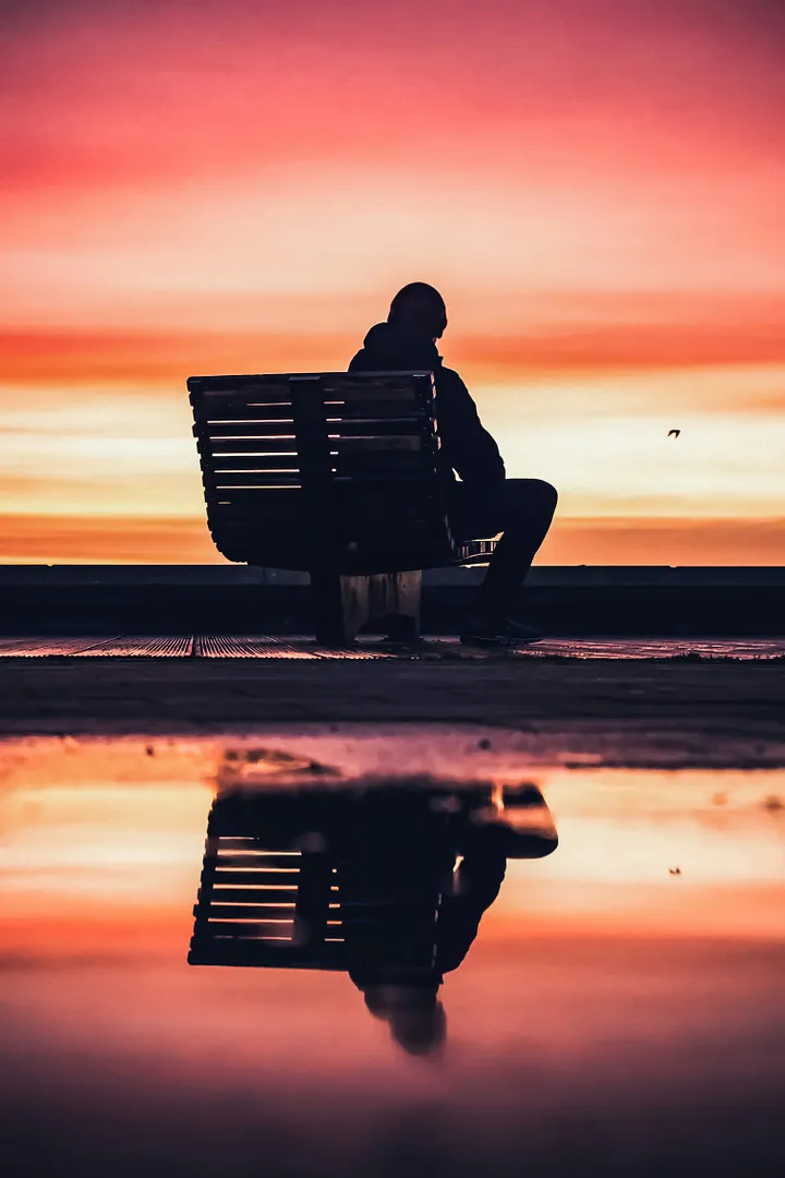 Person reflecting on a bench with a beautiful pink sunset 