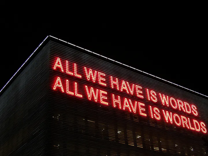 Neon sign that says: All we have is words. All we have is worlds.
